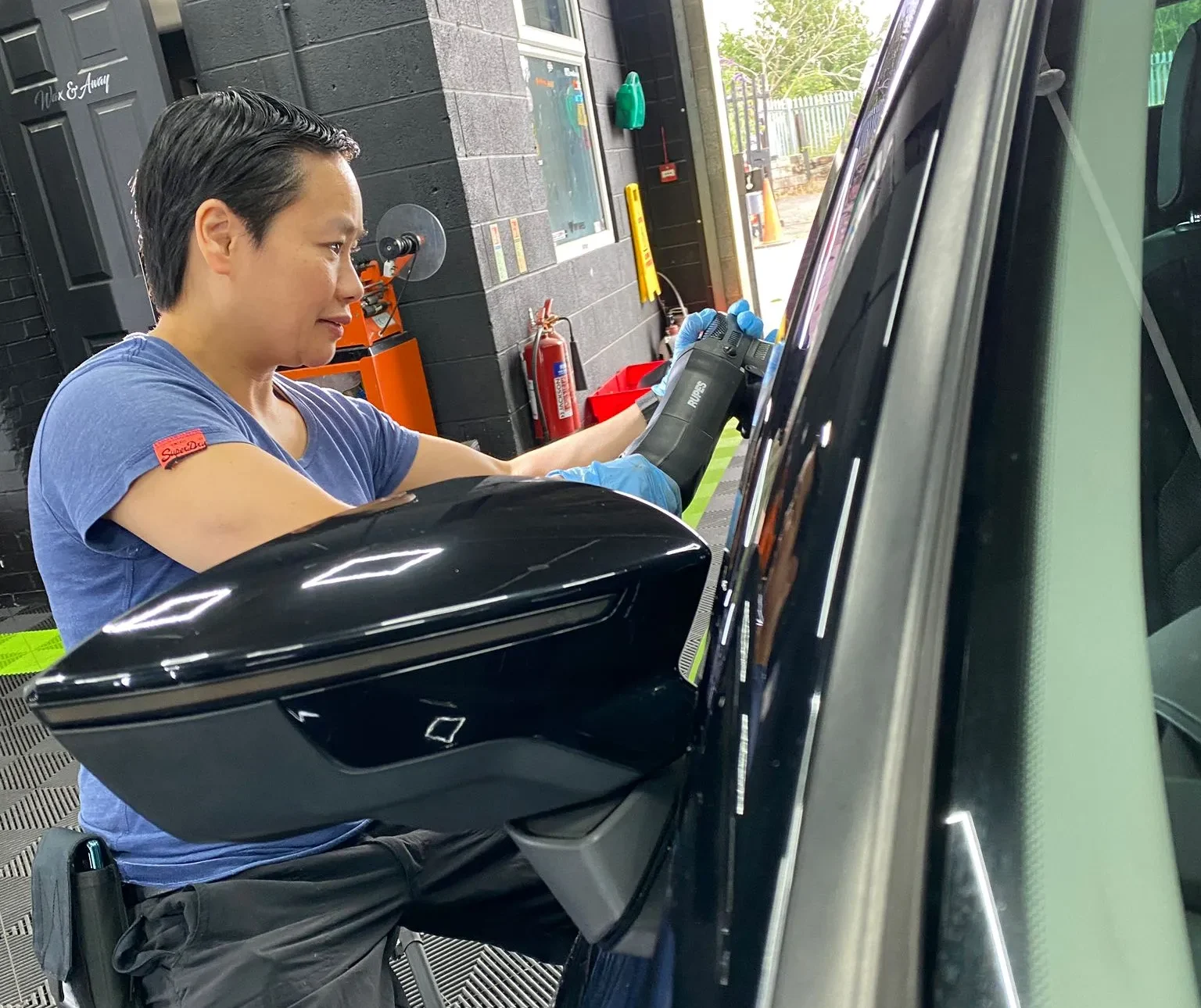 Soo from Hydrowax using a machine polisher on a black car door panel to remove swirl marks